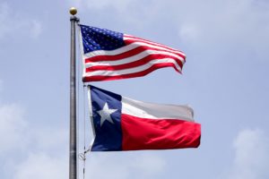 US and Texas flags on a pole against a bright blue sky